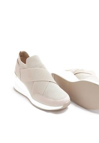 Baskets de sport beige clair avec un mélange de mesh et de tissu lisse, dotées de larges sangles élastiques et d'une semelle compensée blanche, offrant une finition texturée.