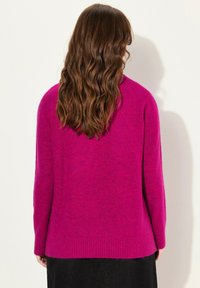 Fuchsia gestrickter Pullover mit bequemer Passform, geripptem Saum und langen Ärmeln. Weiche Textur mit minimalen Details, von hinten betrachtet.
