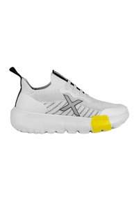 Zapatilla deportiva blanca con parte superior de tejido transpirable, acentos en negro, logo gris, suela blanca gruesa y un detalle en el talón de color amarillo brillante.