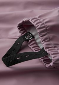Ljusrosa vattentät jacka med elastiska ärmslut, svart justerbar rem med transparent knappdetalj. Slät textur.