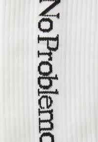 Chaussettes blanches côtelées avec un texte en tricot noir "No Problem" courant verticalement sur un côté. Texture douce avec un design classique.