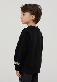 Czarny sweter z ribbowanym dekoltem i mankietami. Posiada logo "Pokémon" na lewym rękawie. Wygodny, casualowy krój.