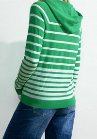 Sweat à capuche rayé vert et blanc avec un tissu texturé et des poignets côtelés, associé à un jean en denim bleu.