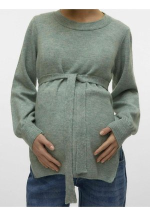 Gravid person iført en blød grøn strikket sweater med bundet bælte, der blidt holder på maven, kombineret med blå jeans.