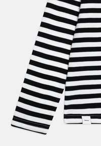 Chemise à manches longues rayée noir et blanc avec une texture douce, présentant une coupe droite et une petite étiquette sur l'ourlet.