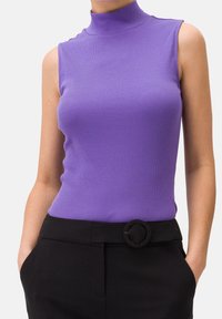 Top viola senza maniche con collo alto e texture a coste. Abbinato a pantaloni neri con una fibbia a forma di rotondo.