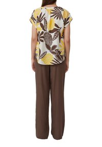 Krótki rękaw blouse z nadrukiem żółtych i brązowych liści, zestawiony z luźnymi brązowymi spodniami. Materiał wydaje się lekki z teksturowanym wykończeniem.