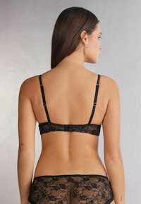 Černá krajková podprsenka s nastavitelnými ramínky a květinovými vzory. Hladký obvod vzadu se zapínáním na háček. Texturovaná krajka zvýrazňuje detaily.