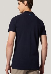 Granatowa koszulka polo z krótkim rękawem, klasycznym kołnierzykiem oraz małym detalem logo z tyłu. Miękki bawełniany materiał o gładkiej fakturze.