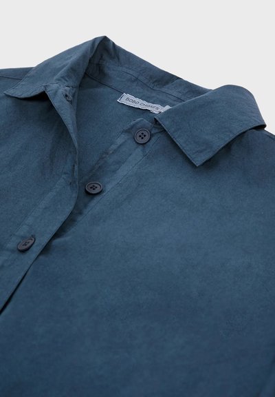 Camicia a maniche corte, con bottoni, di colore blu navy scuro, realizzata in tessuto morbido e testurizzato. Presenta un colletto classico e quattro bottoni neri.