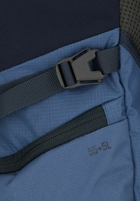 Blauwe rugzaksectie met gestructureerd oppervlak, voorzien van een zwarte sluiting en een label met "55+5L" in de buurt van een zak met donkere accenten.