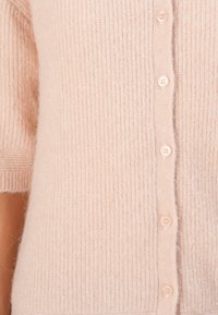 Light pink knitted cardigan made from soft fabric, featuring a ribbed texture and six matching buttons down the front.