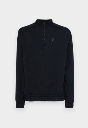 Svart zip-up hettegenser med høy krage, elastiske mansjetter og bunn. Har en diskret logo på brystet. Mykt, teksturert materiale.