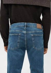 Pantalones vaqueros de mezclilla azul con cintura de talle medio, que cuentan con una parche de cuero en la parte trasera, dos bolsillos traseros y un diseño clásico de cinco bolsillos.