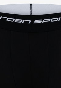 Crne sportske gaćice s mekim pojasom na kojem se ističe bijeli natpis "Jordan Sport". Tkanina izgleda glatko s prilagođenim dizajnom.