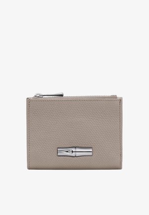Beige leather wallet with a textured finish, silver hardware, and a zip closure. Features a prominent metallic accent on the front.