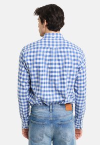 Blå- og hvit rutet skjorte med knapp-ned krage, lange ermer og avrundet kant, kombinert med falmede blå denimjeans.