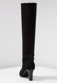 Stivale in suede nero, alta fino al ginocchio, con una forma affusolata, texture liscia e un tacco di 3 pollici. Presenta una semplice cucitura lungo il retro.