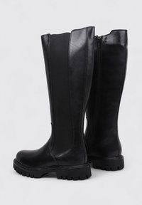 Bottes noires montantes en cuir avec un panneau texturé, fermeture éclair sur le côté et semelle robuste pour l'adhérence. Fini lisse avec un bout arrondi.