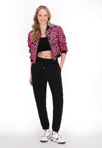 Rosa leopardmønstret bomberjakke, sort crop top, sorte joggers og hvide sneakers. Jakken har ribbede manchetter og en kort silhuet.