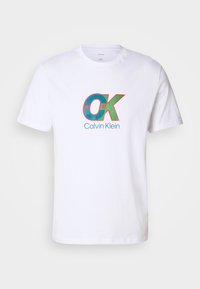 White cotton T-shirt featuring a bold graphic in red and turquoise with "OK" and "Calvin Klein" text at the center. Short sleeves.