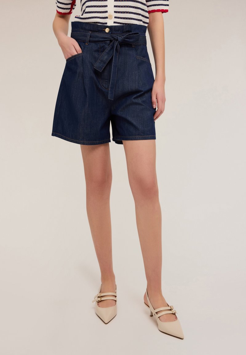 Pantalones cortos de mezclilla en azul oscuro con una cintura alta, piernas anchas, bolsillos frontales y un cinturón de tela a juego. Textura suave y detalles de costura mínimos.
