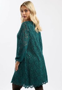 Turkusowa koronkowa sukienka z długimi rękawami, kwiatowymi wzorami, falbaniastym dołem i dekoracyjnymi cekinami. Przezroczysta tekstura dodaje elegancji projektowi.
