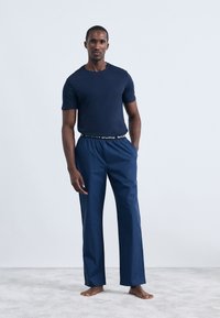 Tamno plavi pamučni majica uparen s prugastim tamnoplave udobnim hlačama s elastičnim pojasom s logotipom. Mekani materijal, opušteni kroj.