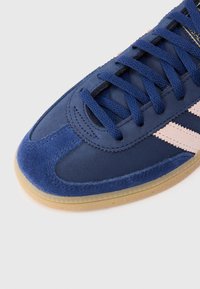 Sapatilhas azul-marinho com acabamento em camurça, sola de borracha texturizada e riscas de destaque em rosa. Apresenta bico arredondado e atacadores largos.