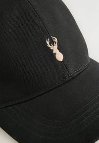 Cappellino da baseball nero realizzato in tessuto testurizzato, caratterizzato da un piccolo logo di un cervo ricamato beige. Visiera curvata e corona strutturata.