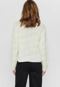 Vit, tjock stickad tröja med en strukturerad mönster, med en kortad design och sänkta axlar. Bakifrån visas minimal detaljering.