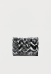 Μαύρο και άσπρο πορτοφόλι με στάμπες, με κλείσιμο flap, λεπτομέρεια χρυσού λογότυπου μπροστά, τοποθετημένο σε απλή ανοιχτόχρωμη φόντο.