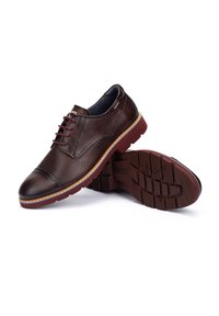 Bruine leren schoenen met een gestructureerd patroon op de bovenkant, ronde neuzen en rode rubberen zolen met een profielpatroon en gestikte accenten.