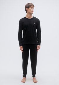 Svart langermet topp og matchende bukser i et glatt, elastisk stoff, med en liten logo på brystet. Tettsittende design med ribbede mansjetter.