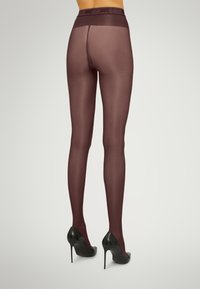 Calze velate bordeaux con texture liscia e una cintura larga. Indossate con scarpe col tacco nere, che mettono in risalto una silhouette aderente.