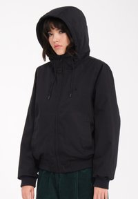 Schwarze Zip-Jacke mit Kapuze, elastischen Bündchen und Saum. Verfügt über Seitentaschen und ein minimalistisches Design ohne sichtbare Logos oder Muster.
