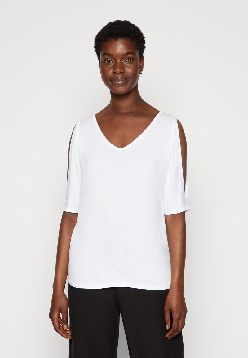 Witte v-hals top met korte mouwen en open schoudernaden, gladde textuur en een ontspannen pasvorm, gecombineerd met zwarte broeken.