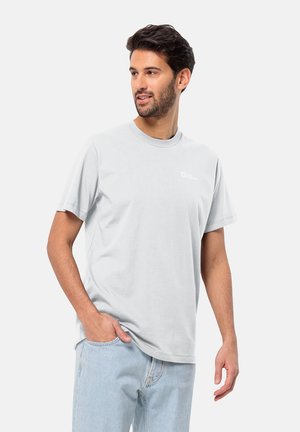 Lichtgrijze katoenen t-shirt met korte mouwen, een ronde hals en een klein wit logo op de borst. Gecombineerd met lichtblauwe jeans.