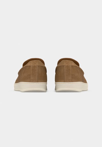 Paire de chaussures à enfiler en daim marron avec semelles en caoutchouc blanc, vues de dos sur un fond gris clair uni.