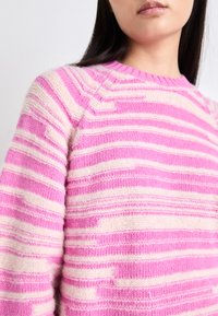 Pull rayé rose et crème avec un tricot texturé, présentant un col rond et des manches raglan. Le design montre des bandes de couleur alternées.