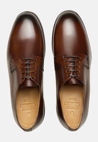 Chaussures de ville en cuir marron avec une finition lisse, bout arrondi et fermeture à lacets. Présente des coutures discrètes et un logo en relief sur la semelle intérieure.