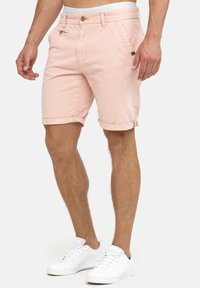 Shorts en denim rose clair avec ourlets retroussés, poches avant et fermeture à bouton. Portés avec des baskets blanches.