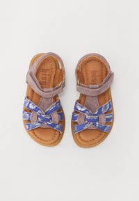 Lilla og blå sandaler til barn med kryssremmer, som har en myk skinnlignende overdel, en teksturert detalj og en polstret tan fotseng.