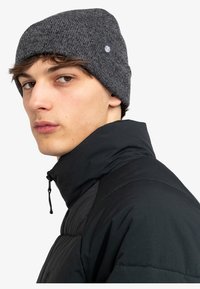 Berretto a maglia grigio con un motivo testurizzato, design aderente e una piccola toppa con logo. Indossato con un giubbotto imbottito nero con colletto alto.