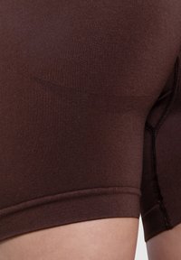 Shorts sportivi marroni realizzati in un tessuto elasticizzato, caratterizzati da una superficie liscia, orlo cucito e lati senza cuciture per garantire comfort durante il movimento.