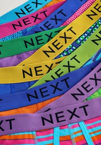 Ceintures élastiques colorées avec une marque "NEXT" en noir. Des motifs variés incluent des rayures, des pois et des designs géométriques sur diverses couleurs.