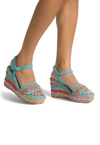 Sandales compensées colorées avec un tissu tressé en rose, jaune, bleu et vert. Présentent des brides à la cheville et un design à bout ouvert.