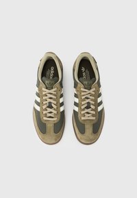 Vihreät mokka- ja verkkokangaslenkkarit, joissa on kolme valkoista raitaa, beiget nauhat ja kumipohja. Kenkäparissa on pehmustettu kaulus ja kieli.