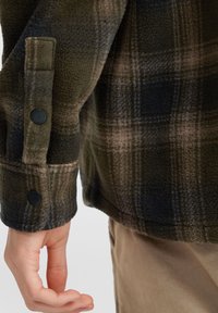 Børstet uld flannel-skjorte i grøn, brun og sort med sorte trykknapper. Blød tekstur med en afslappet pasform og synlige syninger.