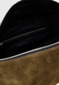 Interno di una borsa in suede color beige con foderatura in tessuto nero. Presenta una tasca con zip e una chiusura a zip liscia lungo la parte superiore.